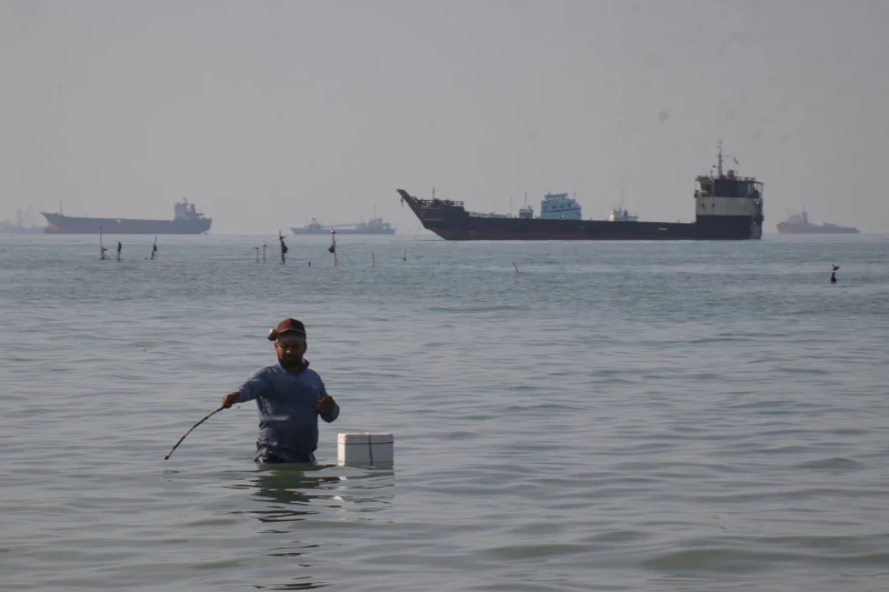 Un hombre se encuentra en el mar, aparentemente pescando, mientras buques de carga y de otro tipo pueden verse en el horizonte del estrecho de Ormuz, el lunes 27 de abril de 2026, frente a la costa de Bandar Abbas, Irán.