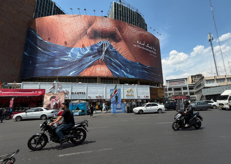 Vehículos circulan junto a una valla publicitaria con una imagen del estrecho de Ormuz y los labios cosidos del presidente estadounidense Donald Trump, en una plaza del centro de Teherán, Irán, el sábado 2 de mayo de 2026.