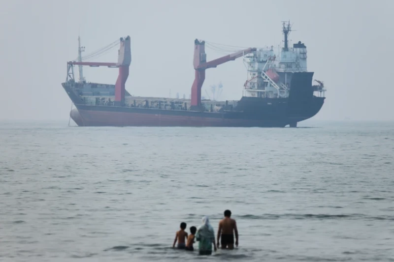 Varias personas se meten en el agua en la orilla mientras un carguero aparece fondeado en el estrecho de Ormuz, ante la costa de Bandar Abbas, Irán, el 30 de junio de 2026.
