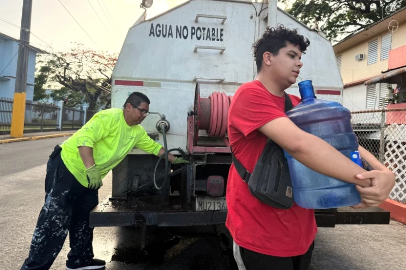 Bryan Pérez carga un bidón de agua de cinco galones hacia su apartamento en el complejo de vivienda pública Villa Kennedy, en San Juan.