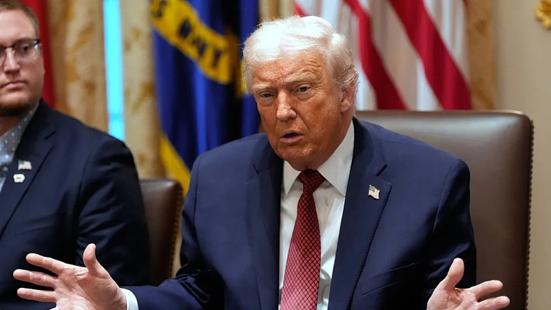 Donald Trump aparece de pie, con gesto serio y ligeramente inclinado hacia delante.