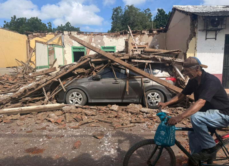 Un hombre pasa en bicicleta frente a una casa derrumbada y un coche enterrado bajo escombros en la localidad de Chitre, a unos 250 km al suroeste de Ciudad de Panamá, el 10 de octubre de 2026.