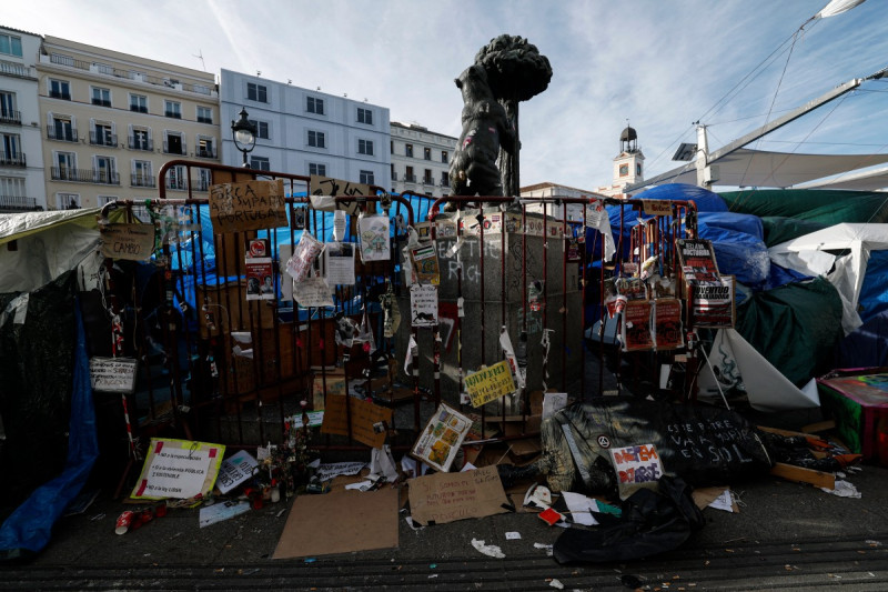 Se observan barreras cubiertas de mensajes desgastados y escombros frente a la icónica estatua del oso en la Puerta del Sol, en Madrid, donde el 23 de octubre de 2026 permanecen acampados manifestantes que protestan contra la crisis de la vivienda.
