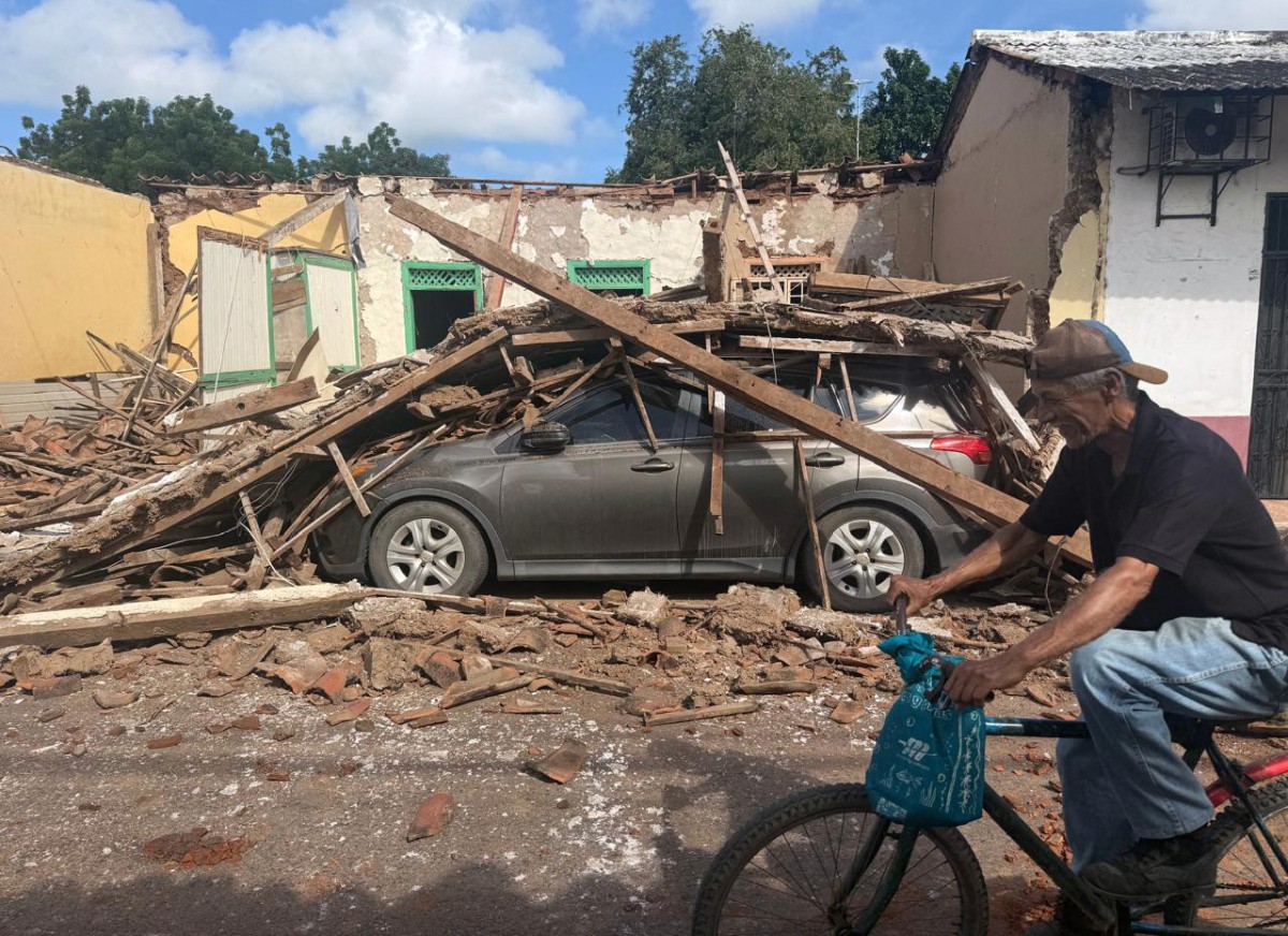 Un hombre pasa en bicicleta frente a una casa derrumbada y un coche enterrado bajo escombros en la localidad de Chitre, a unos 250 km al suroeste de Ciudad de Panamá, el 10 de octubre de 2026.