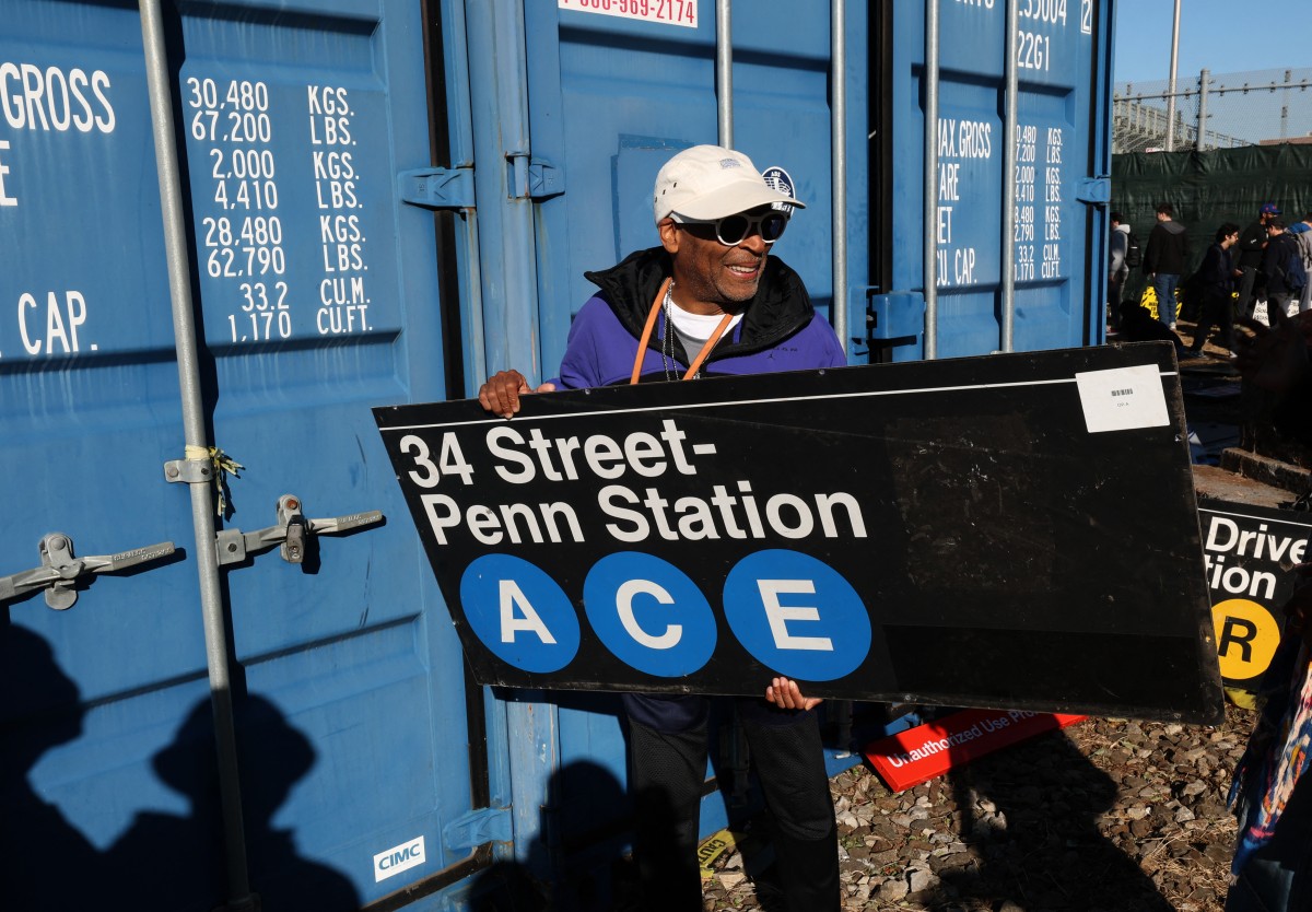 El director de cine Spike Lee sostiene un letrero del metro mientras la gente se lleva a casa una pieza del sistema de transporte de la ciudad de Nueva York durante la venta temporal anual de NYC Transit.